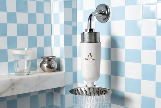 Care Dale filter on a running shower arm, beside a glass with a white limescale ring and a steel lota on a marble ledge