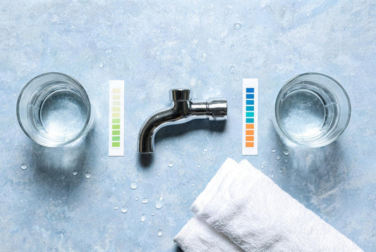 Overhead flat-lay of two glasses of Mumbai tap water, hardness colour charts and a chrome bathroom tap
