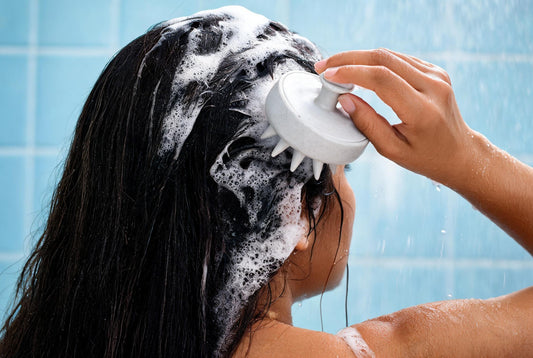 Woman using the Care Dale scalp massager on shampoo-lathered dark hair in the shower