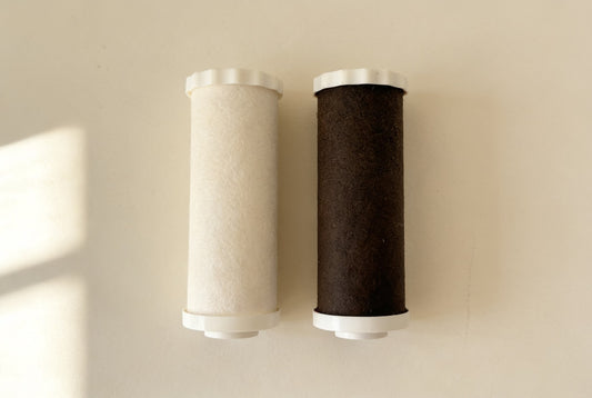 A new off-white shower filter cartridge beside a spent dark brown one after months on hard water